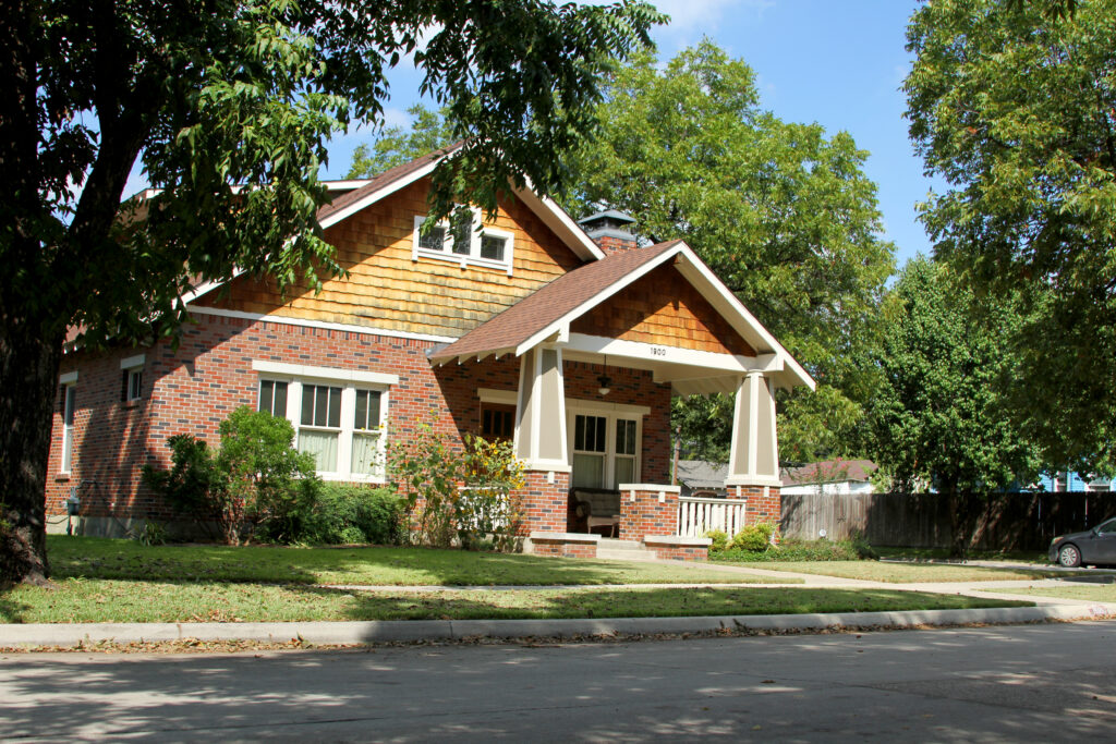 Red brick Craftsman bungalow with a shingled gable and deep front porch in the Fairmount Historic District, Fort Worth, Texas