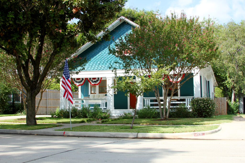 Teal-painted bungalow with a white columned front porch and American flag in the Fairmount Historic District, Fort Worth, Texas