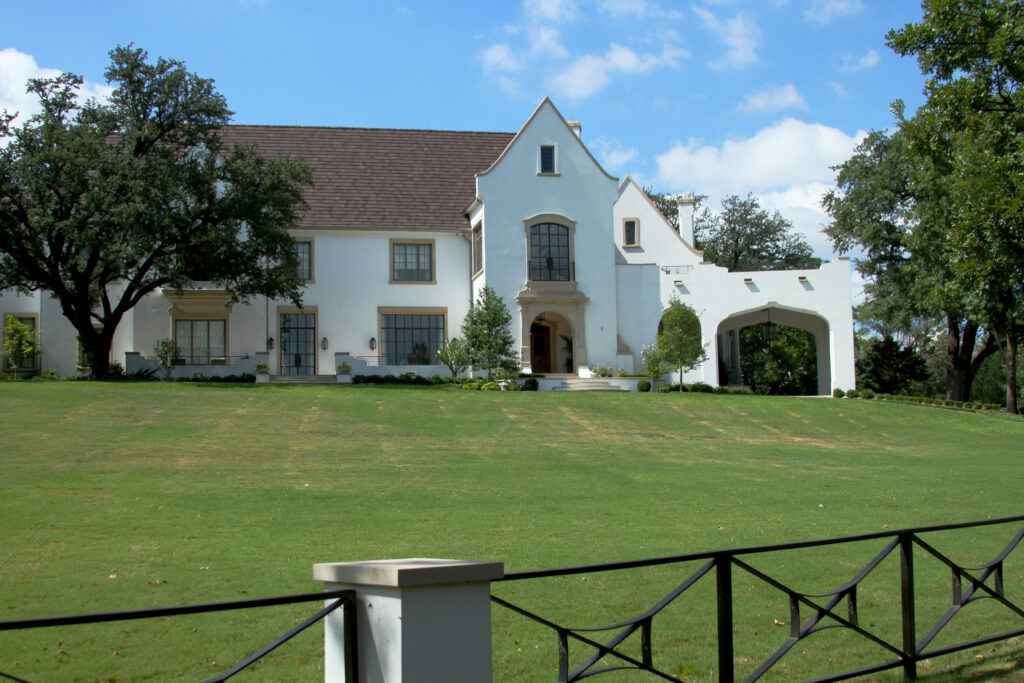 White two-story home with a steep gabled roof set back behind a wide front lawn in the Rivercrest area of Fort Worth, Texas